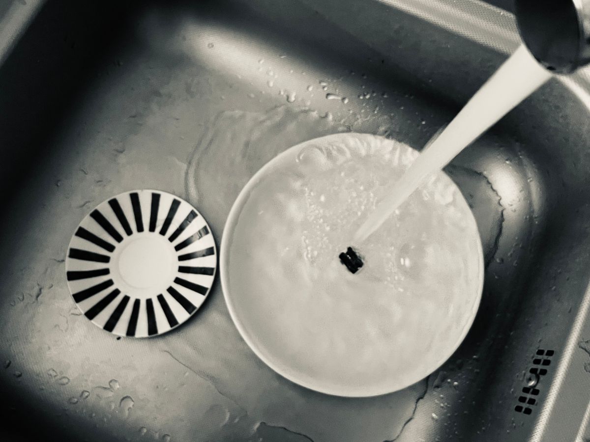 Monochrome view of kitchen sink with dishes being washed under running water