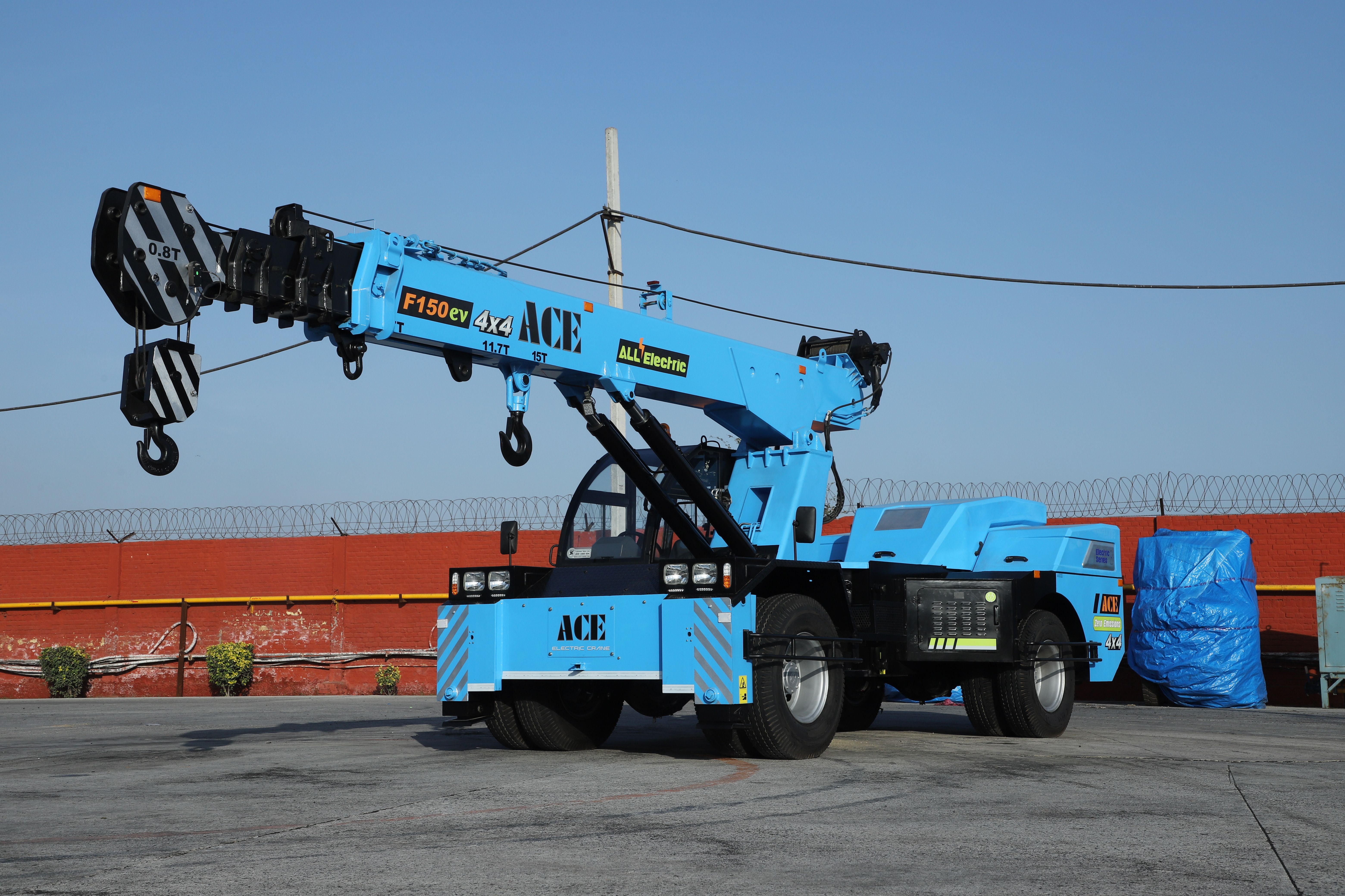 A vibrant blue ACE F150EV electric crane in an outdoor industrial setting in India.