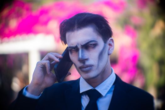 Man in Halloween makeup talking on phone outdoors with vibrant background.