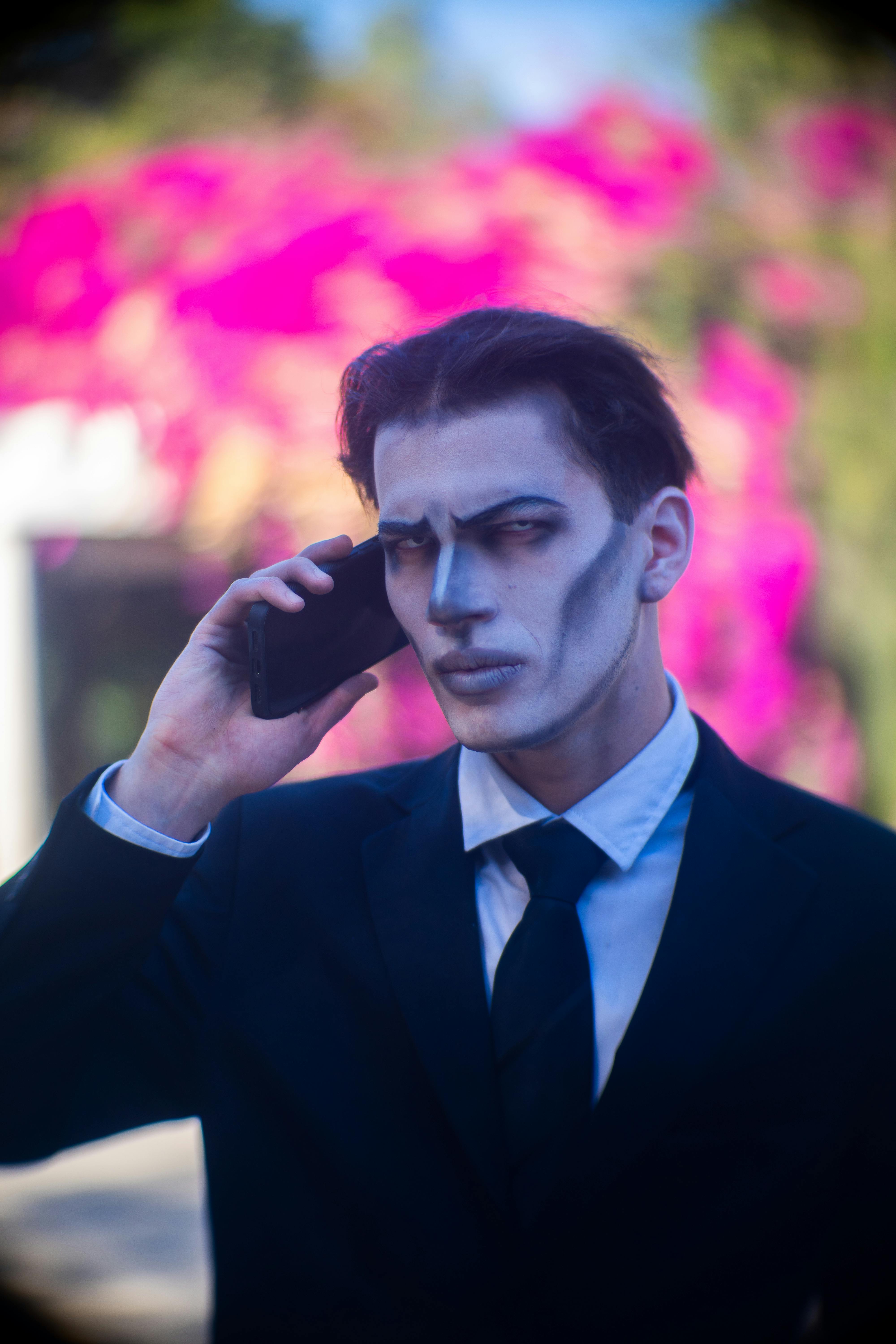 Gratis Hombre con traje y maquillaje gótico haciendo una llamada telefónica al aire libre. Fondo vibrante. Foto de stock