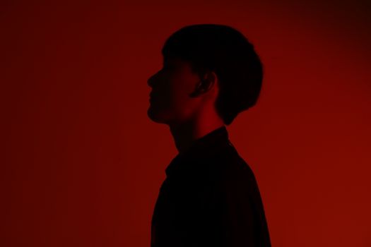 Silhouette of an adult in profile viewed against a red backdrop, creating a moody effect.