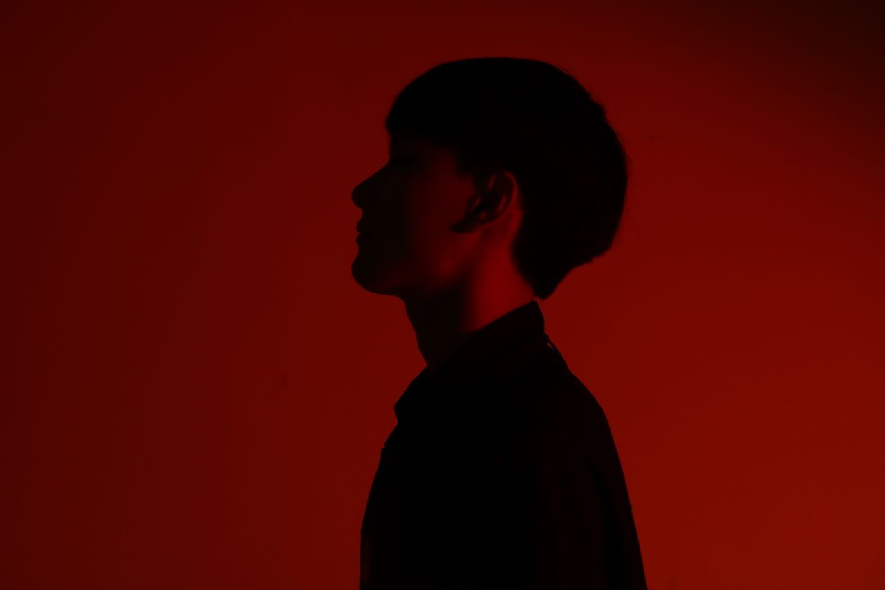 silhouette of an adult in profile viewed against a red backdrop creati