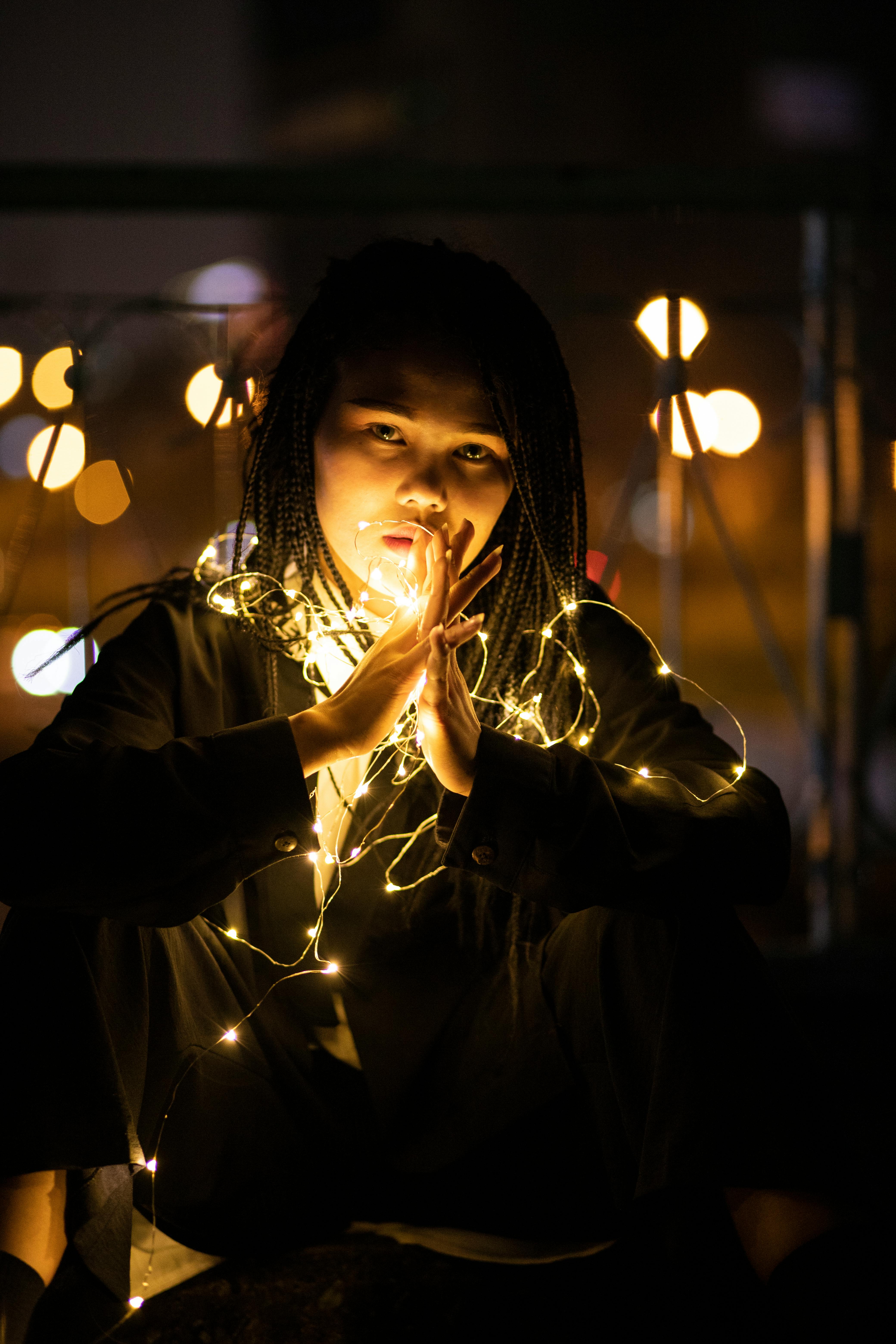 無料 光り輝くイルミネーションに囲まれた女性の、物憂げなポートレート。ドラマチックな夜の雰囲気を醸し出している。 写真素材