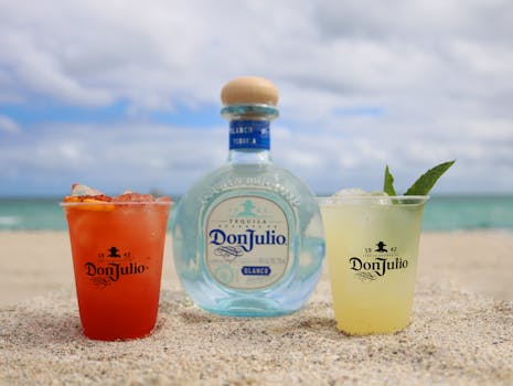 Colorful cocktails and a tequila bottle on a sunny beach setting.