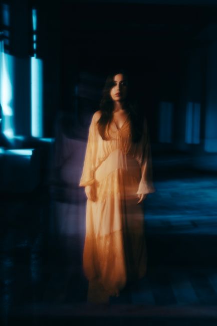 A mysterious woman in flowing attire in a dimly lit, captivating room.