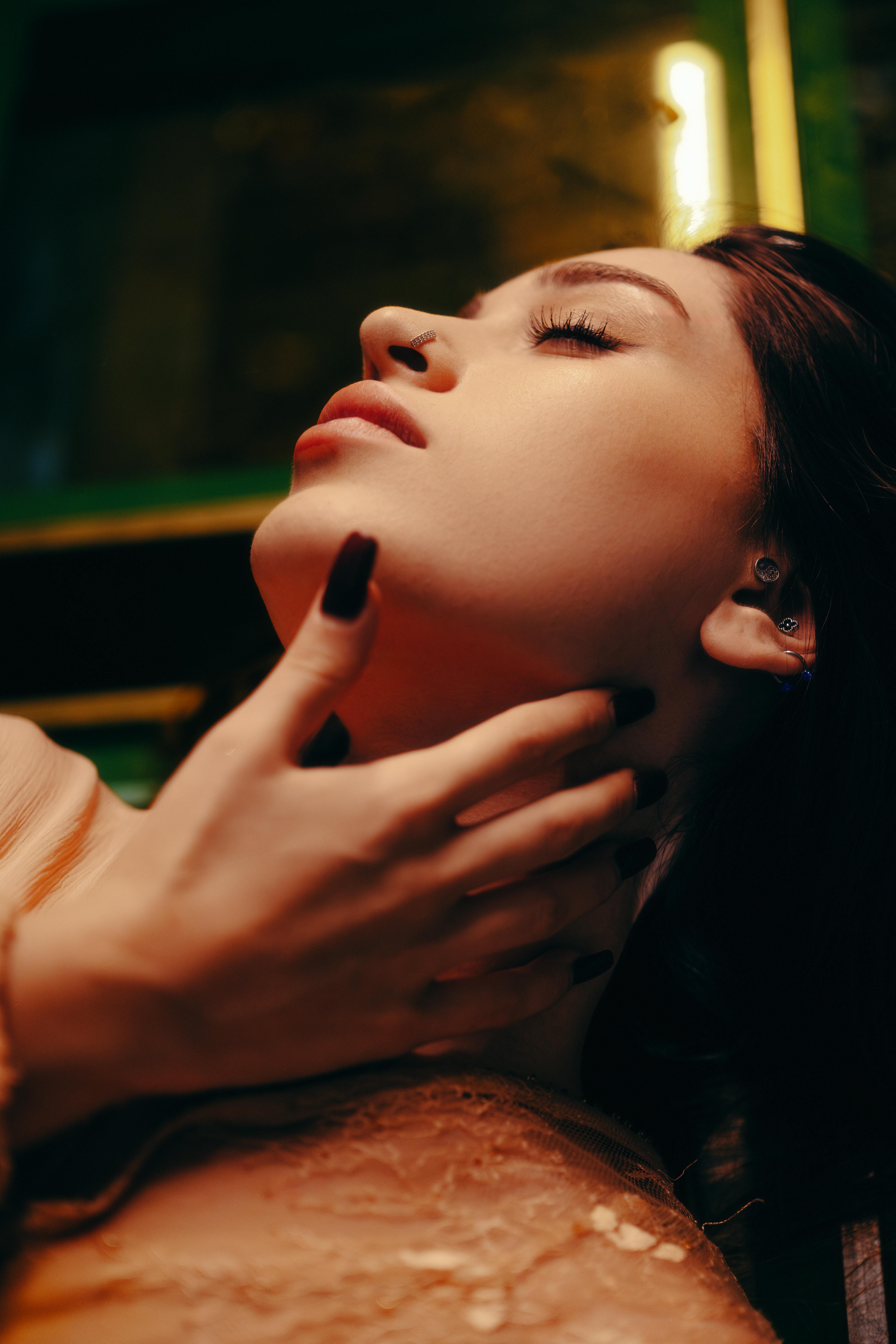 Artistic portrait of a woman with eyes gently closed, face relaxed in deep calm and sensual trance, soft moody lighting highlighting surrender