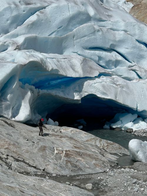 Free Hiker explores stunning ice cave with grand glacier backdrop, capturing natural beauty and adventure. Stock Photo