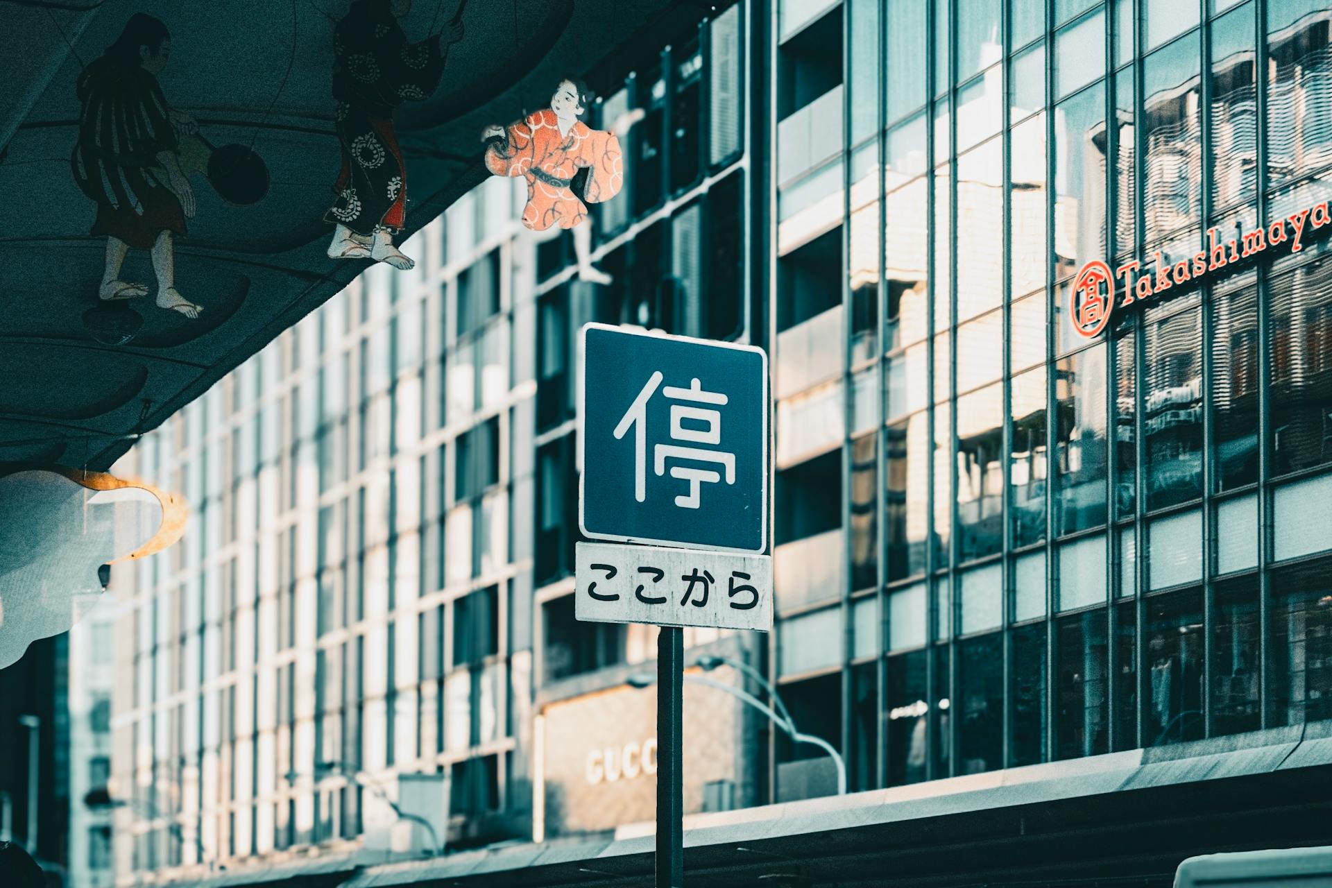 Japanese street sign in busy urban setting, reflecting modern architecture.