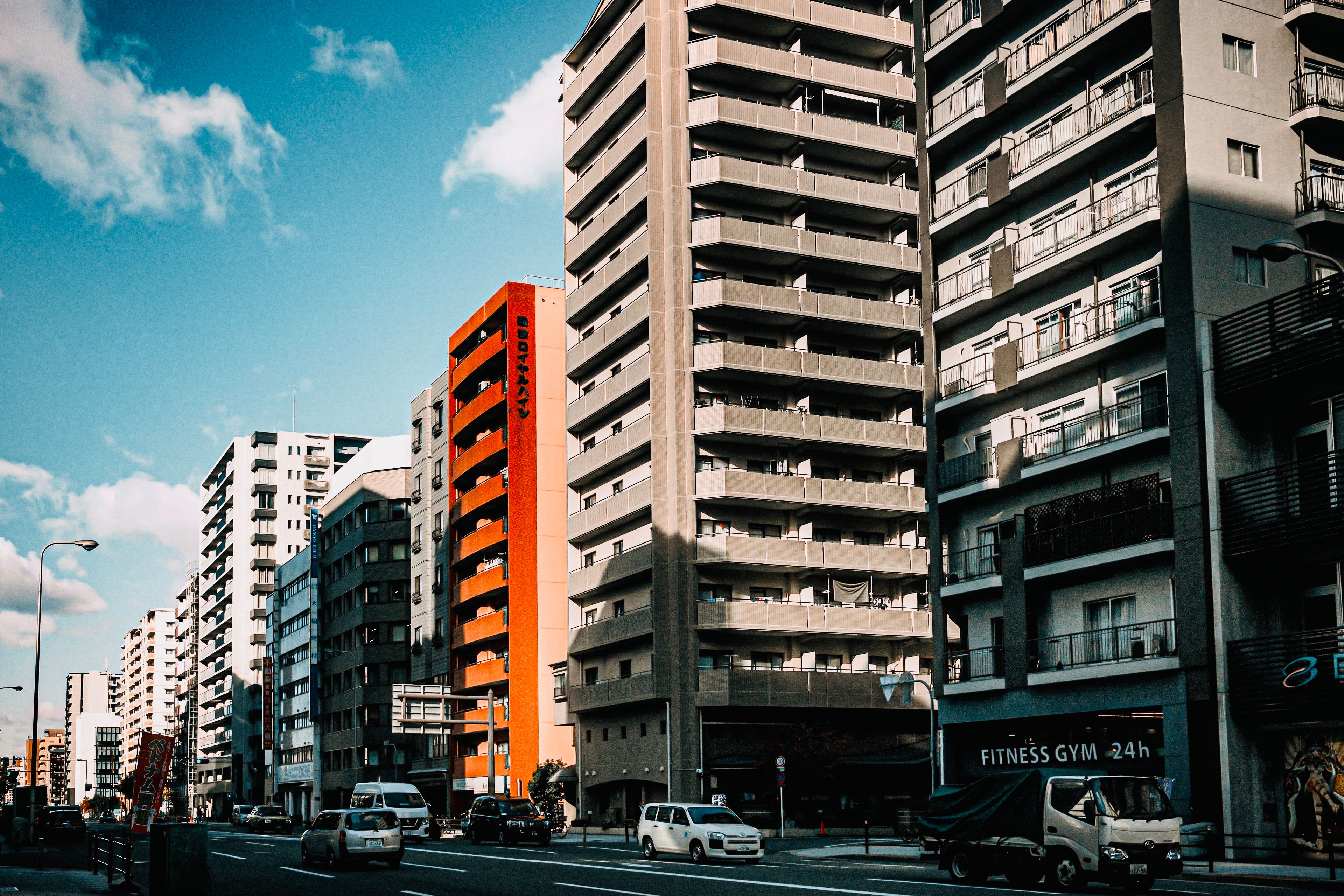 Modern high-rise buildings line a bustling urban street under a bright blue sky.