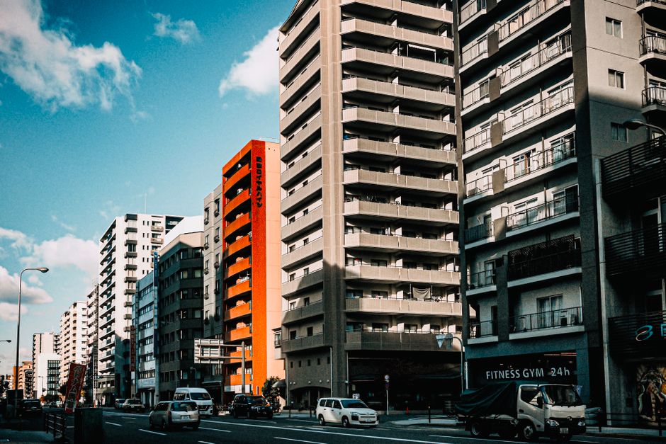 Modern high-rise buildings line a bustling urban street under a bright blue sky.