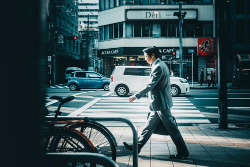Free Businessman in suit crossing street in vibrant city setting. Stock Photo