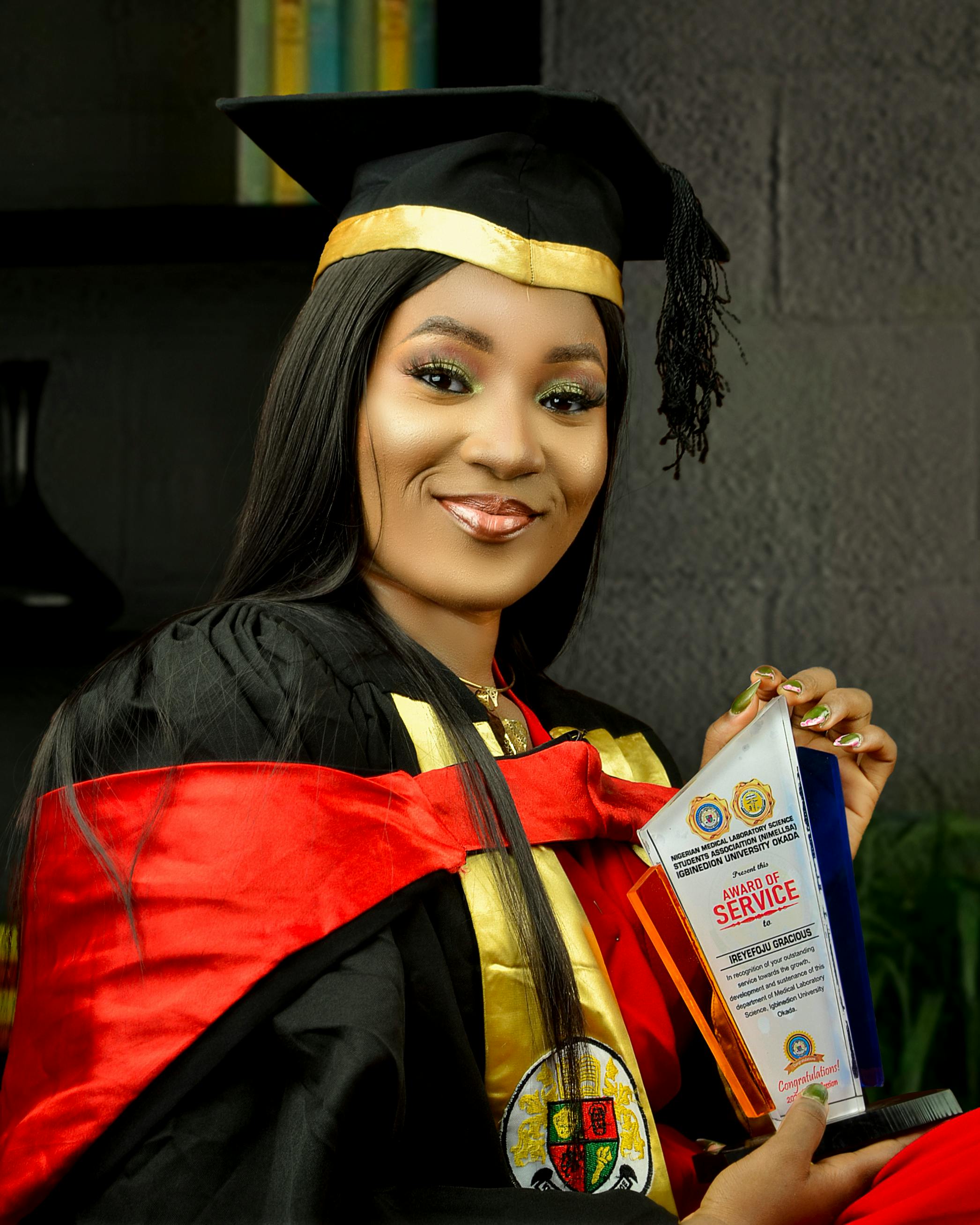 Young woman in a graduation gown holding a service award smiling.