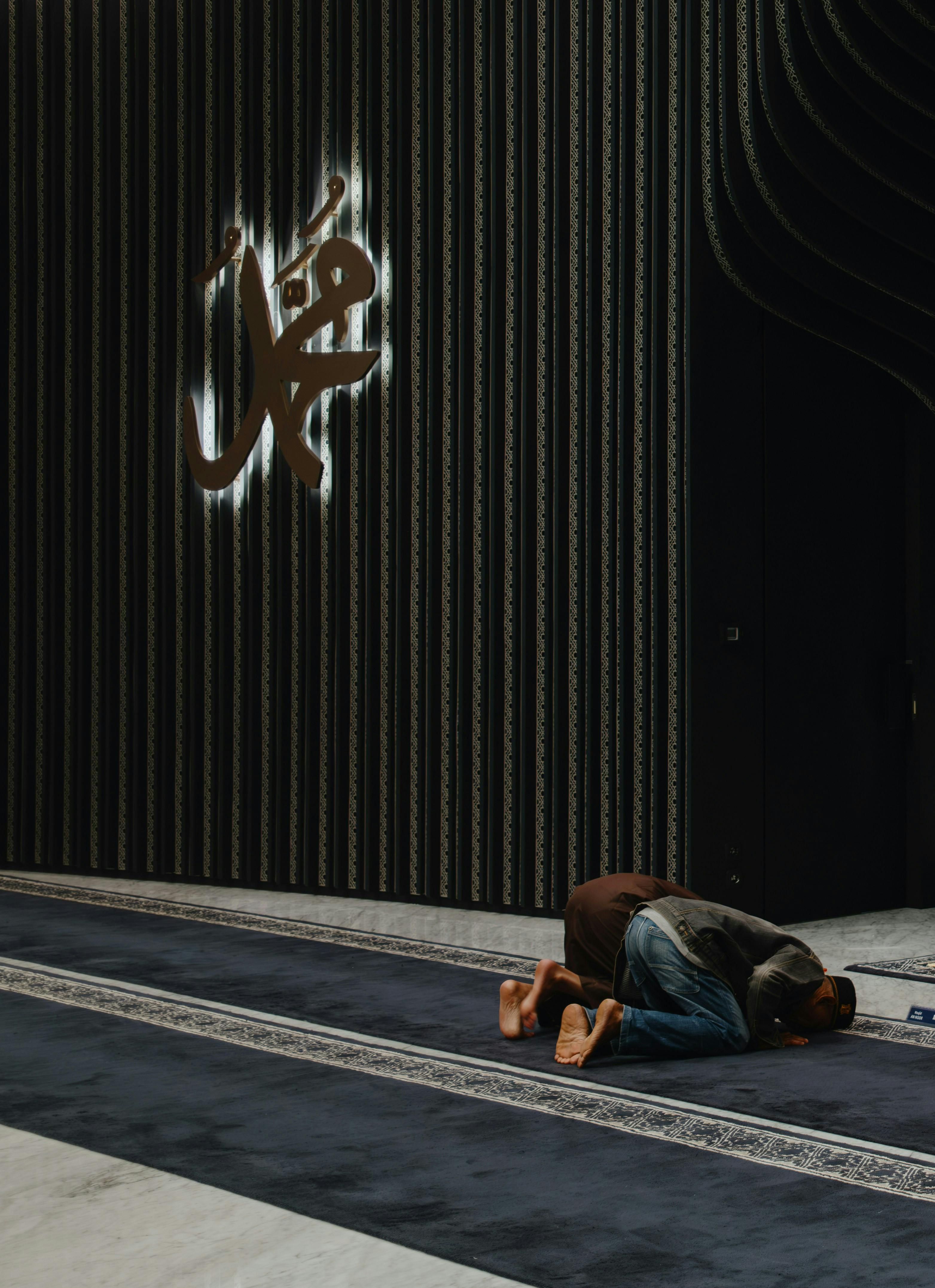 A devotee praying inside a beautifully designed Indonesian mosque showcasing islamic calligraphy.
