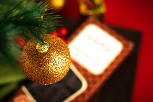 A close-up of a sparkling gold Christmas ornament hanging on a green tree branch with a festive backdrop.