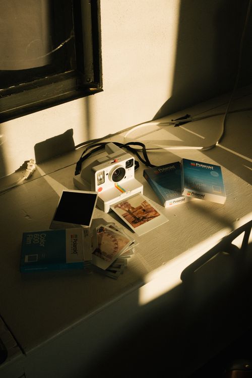 Free A vintage instant camera set on a sunlit desk with film packs and photographs. Stock Photo