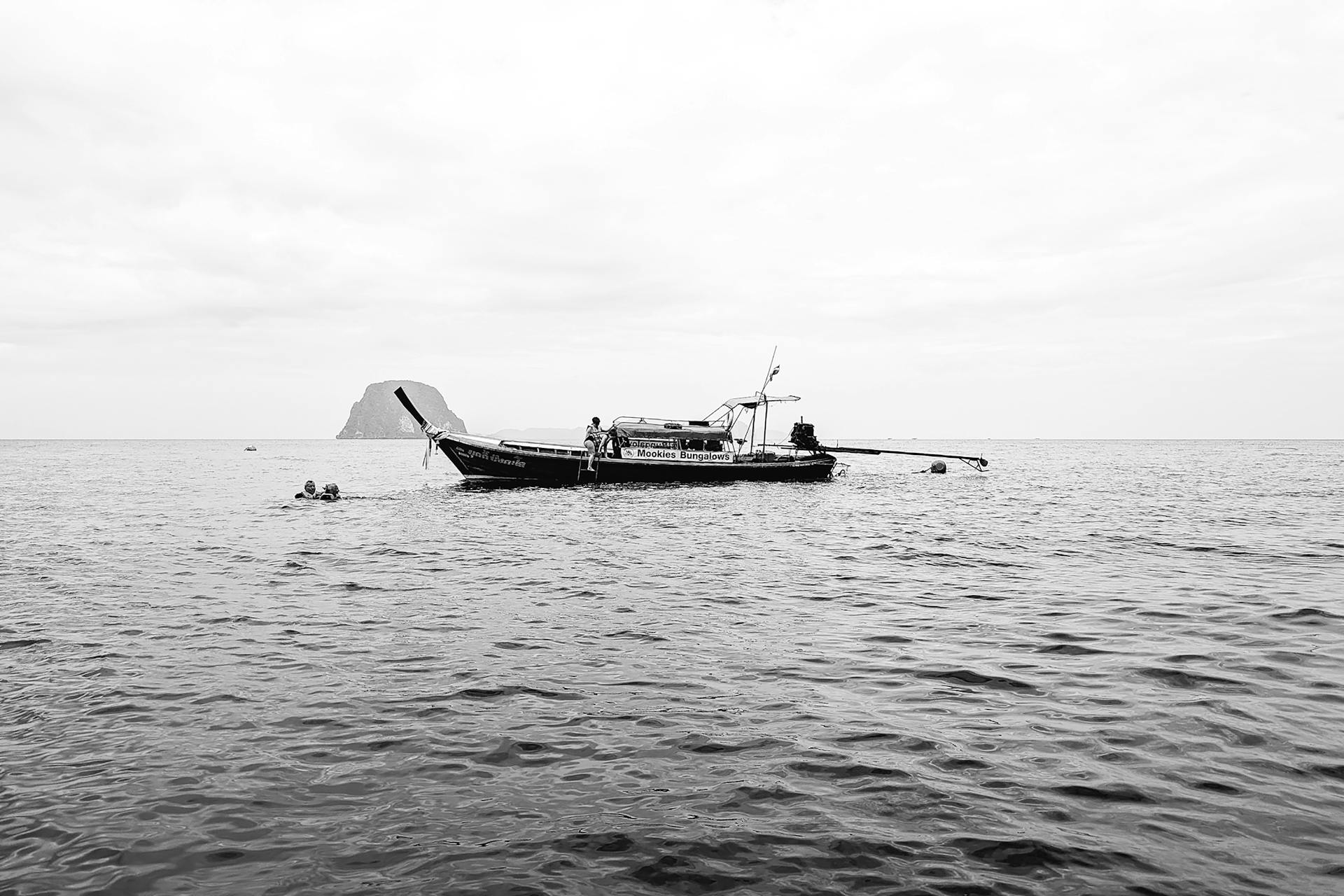 Black and white photo of a longtail boat in calm waters, showcasing serene travel and nature vibes.