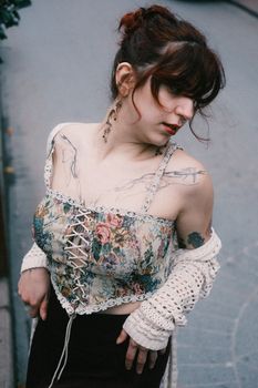 Young woman in floral lace corset and crochet cardigan posing outdoors with vintage style.