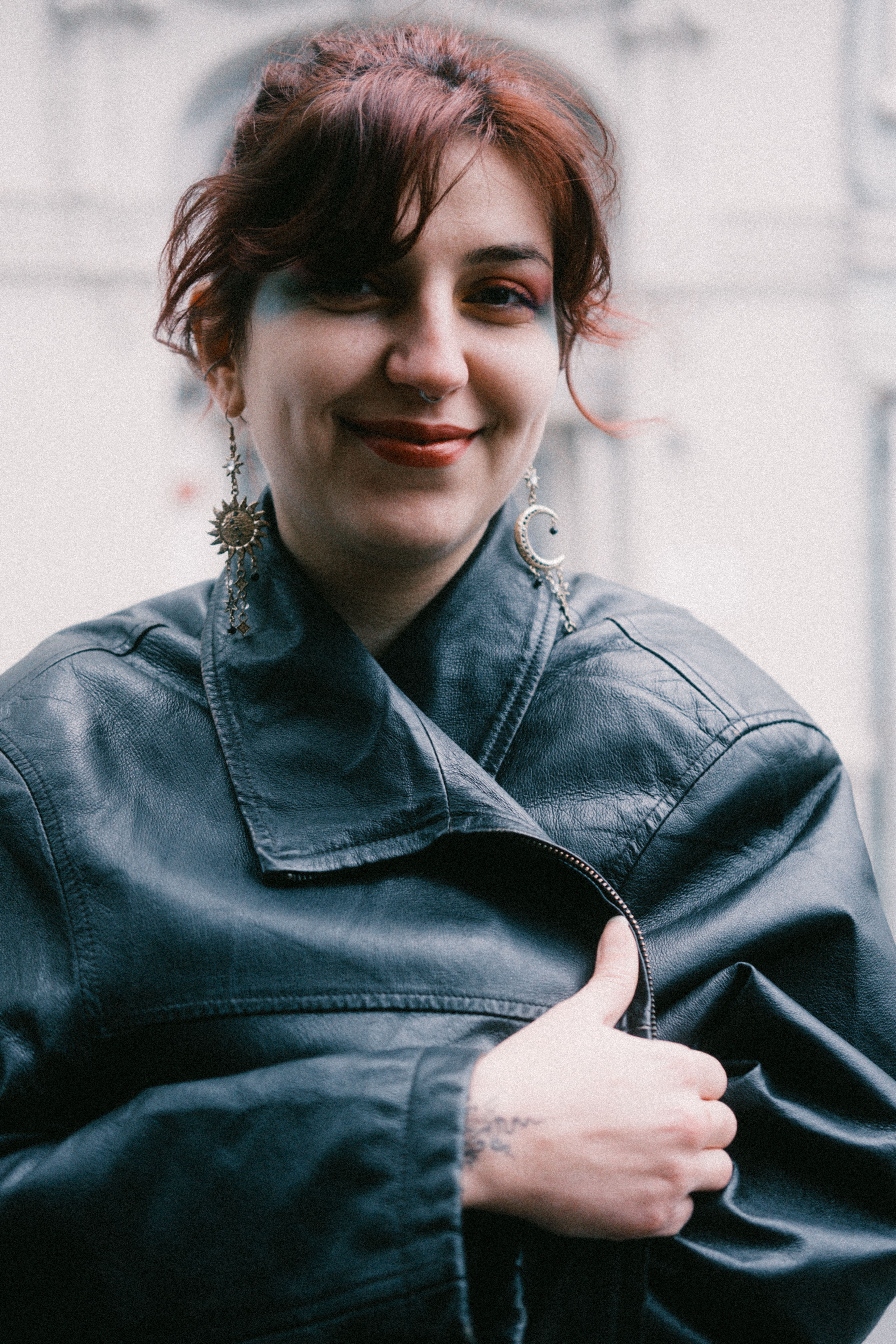 Smiling woman with earrings and black leather jacket in an outdoor setting.