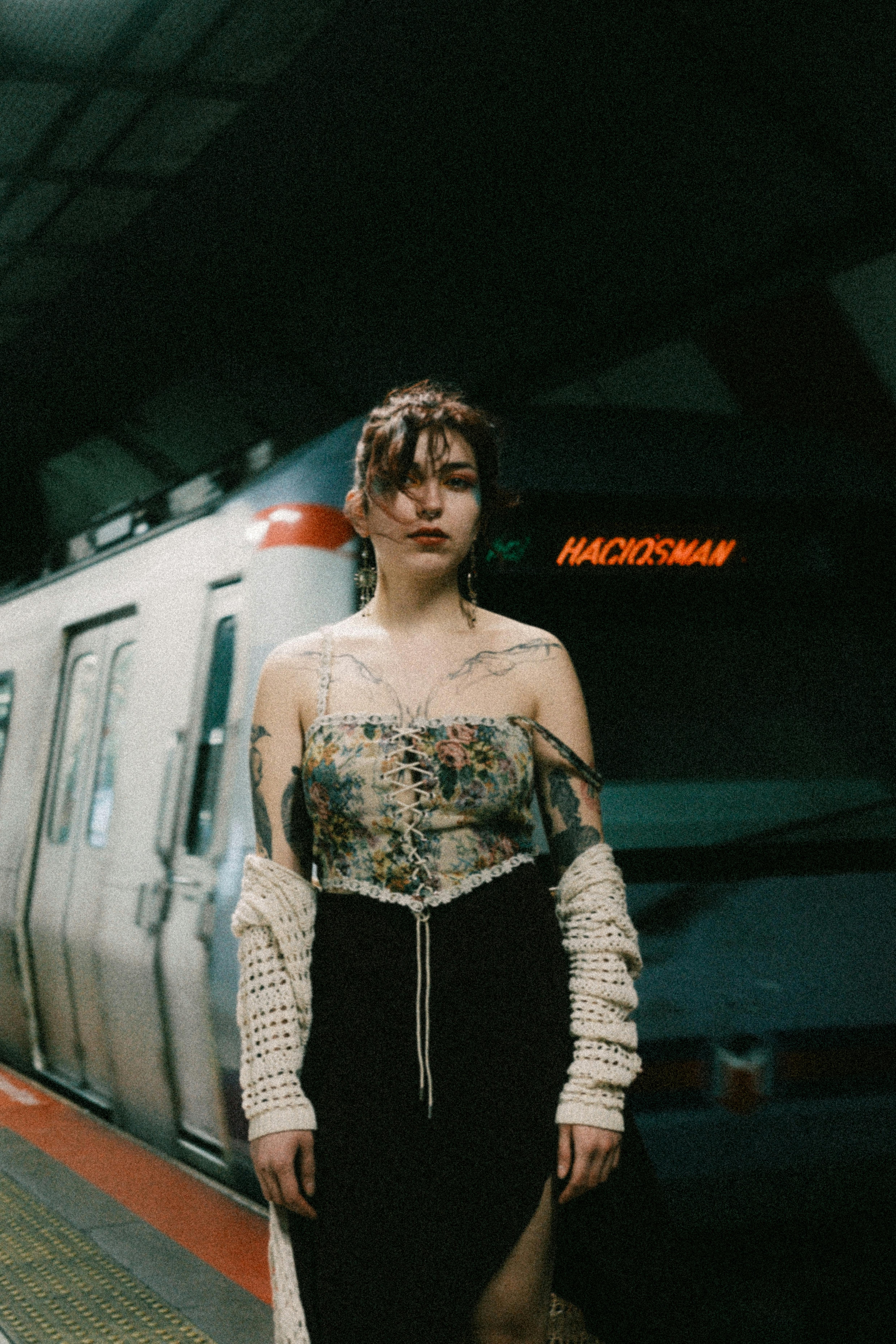 A young woman poses in front of a subway train at night, showcasing a stylish look.