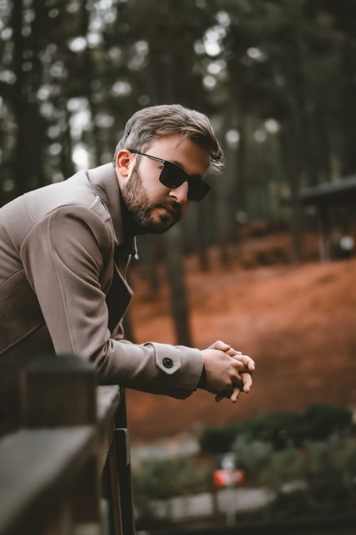 Free Man in sunglasses and coat leaning on railing in a forest setting outdoors. Stock Photo