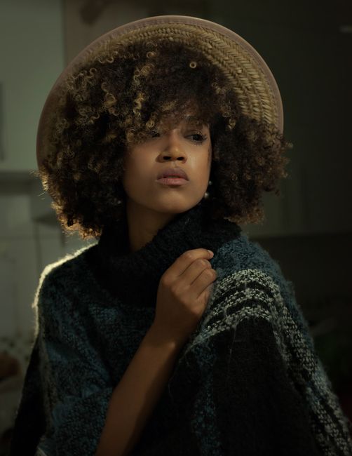 Artistic portrait of a woman wearing a hat and cozy knitwear indoors, showcasing style and fashion.