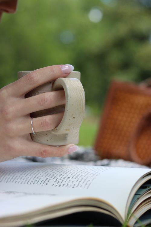 Free Hand holding a ceramic mug over a book for a relaxing outdoor moment. Stock Photo
