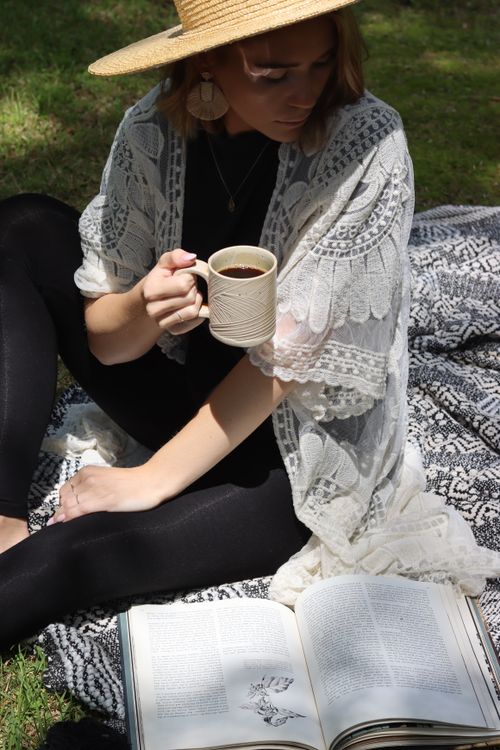 Free A woman enjoys coffee and reading outdoors in a serene bohemian setting. Stock Photo
