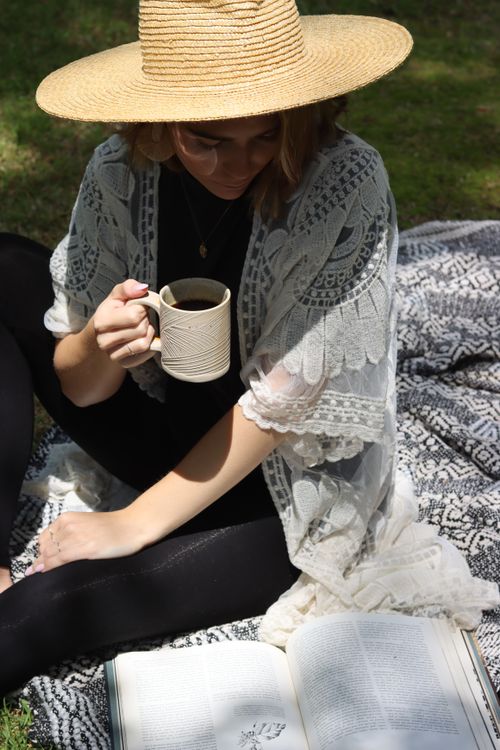 Free Woman enjoying coffee and reading a book in the sun, embodying bohemian spring vibes. Stock Photo