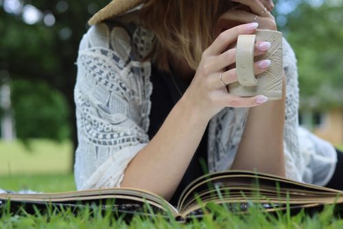Free Woman enjoying coffee and a book outdoors in a serene spring setting. Stock Photo