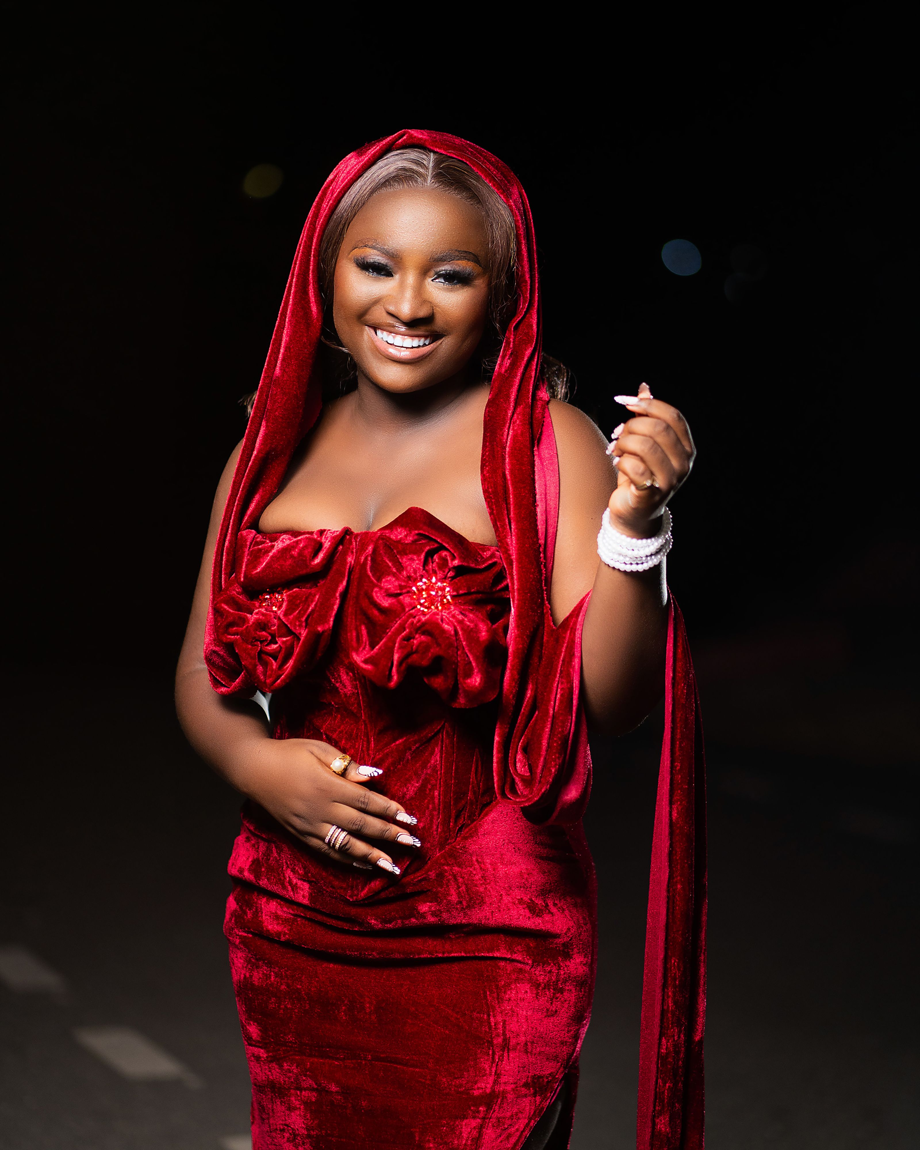 A stylish woman wearing a red velvet dress poses outdoors at night, exuding elegance and confidence.