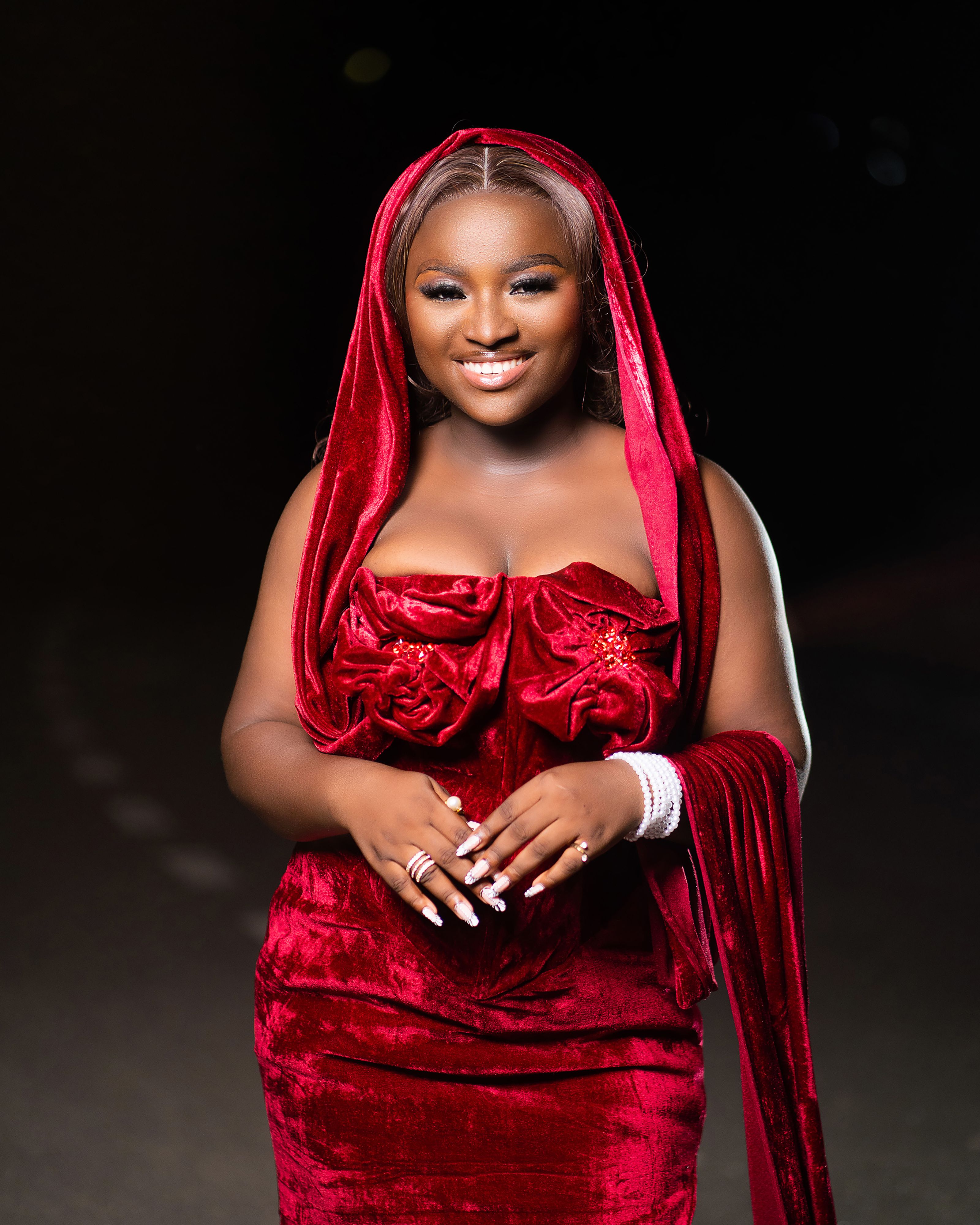A woman posing confidently outdoors at night in a glamorous red velvet dress with hood.
