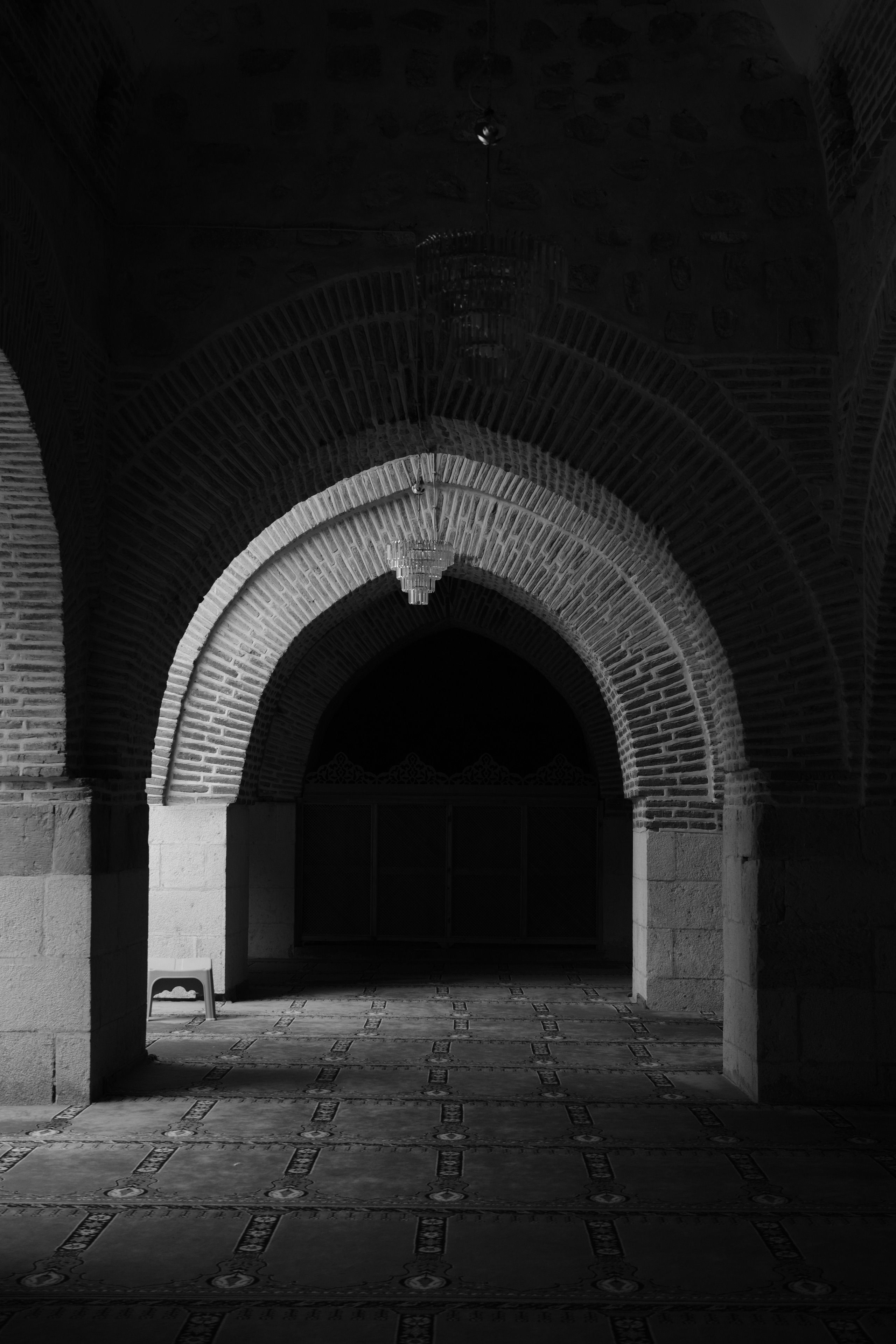 Black and white image of a historical arched hallway with intricate patterns and muted lighting.