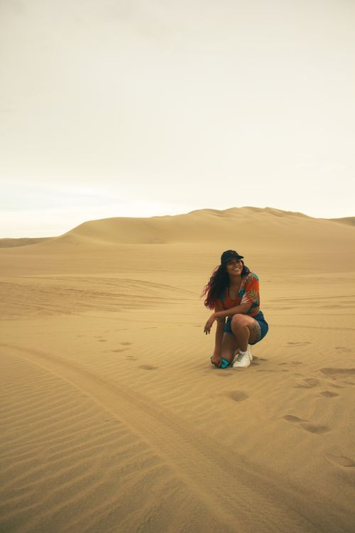 Free A woman kneels in a vast, serene desert landscape at sunset, creating a picturesque scene. Stock Photo