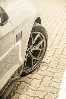 A close-up of a sports car wheel and emblem on a paved surface.