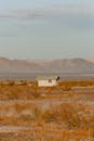 一座孤零零的房子坐落在干旱的沙漠景观中，远处是连绵的山脉