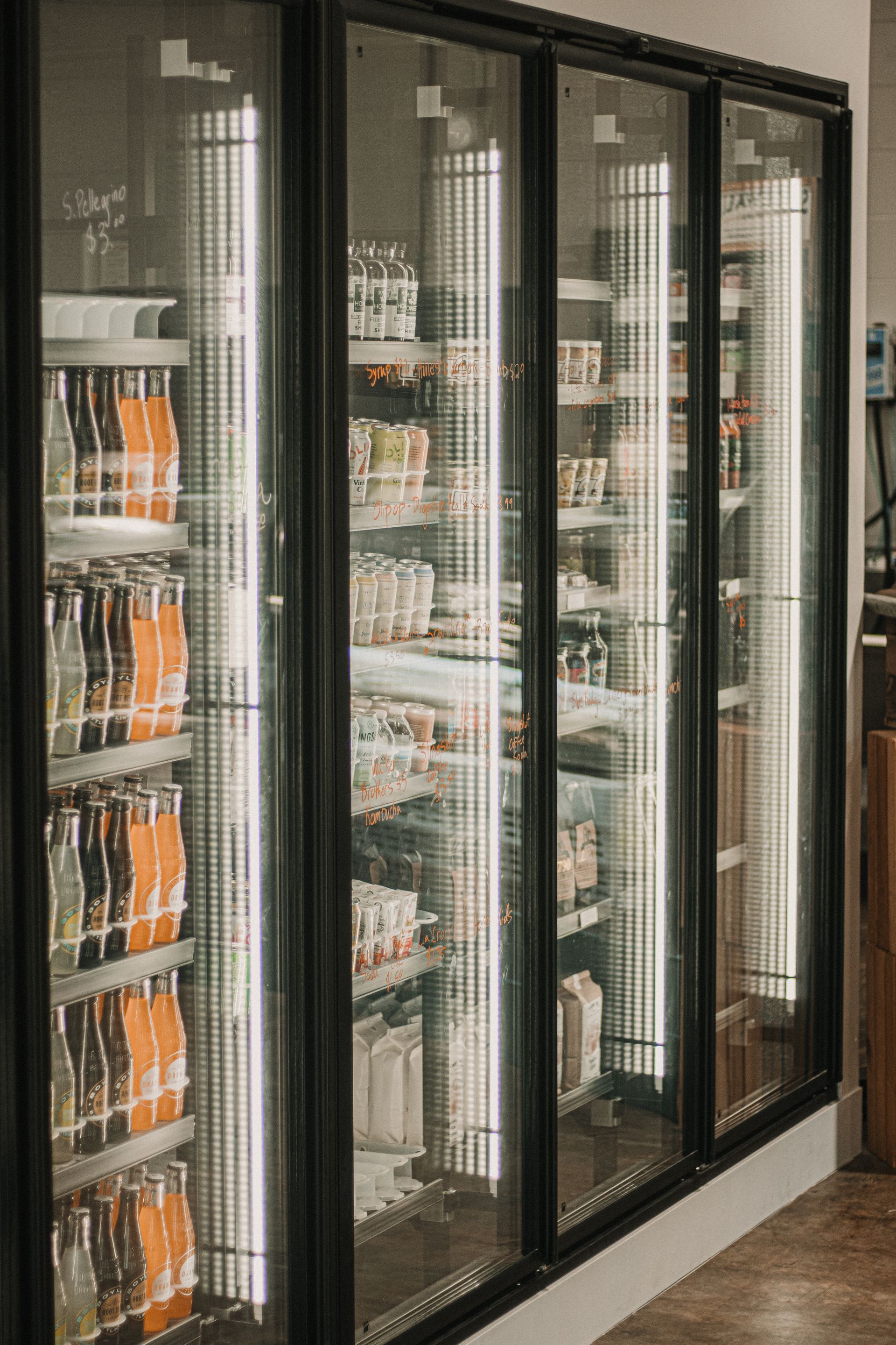 A well-organized beverage and deli section in a grocery store with bright lighting and glass doors