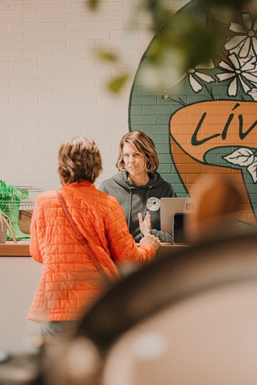 Free Woman conversing with shop attendant in a lively market environment. Stock Photo Free Woman conversing with shop attendant in a lively market environment. Stock Photo