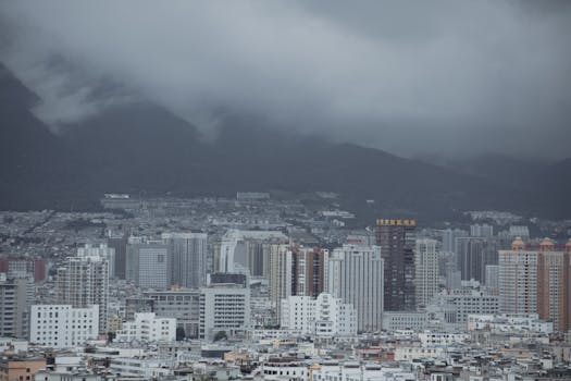 Overcast cityscape view with towering buildings and misty mountains in the background.