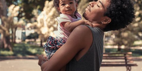 A father joyfully embraces his daughter in a sunny park, capturing a tender moment.