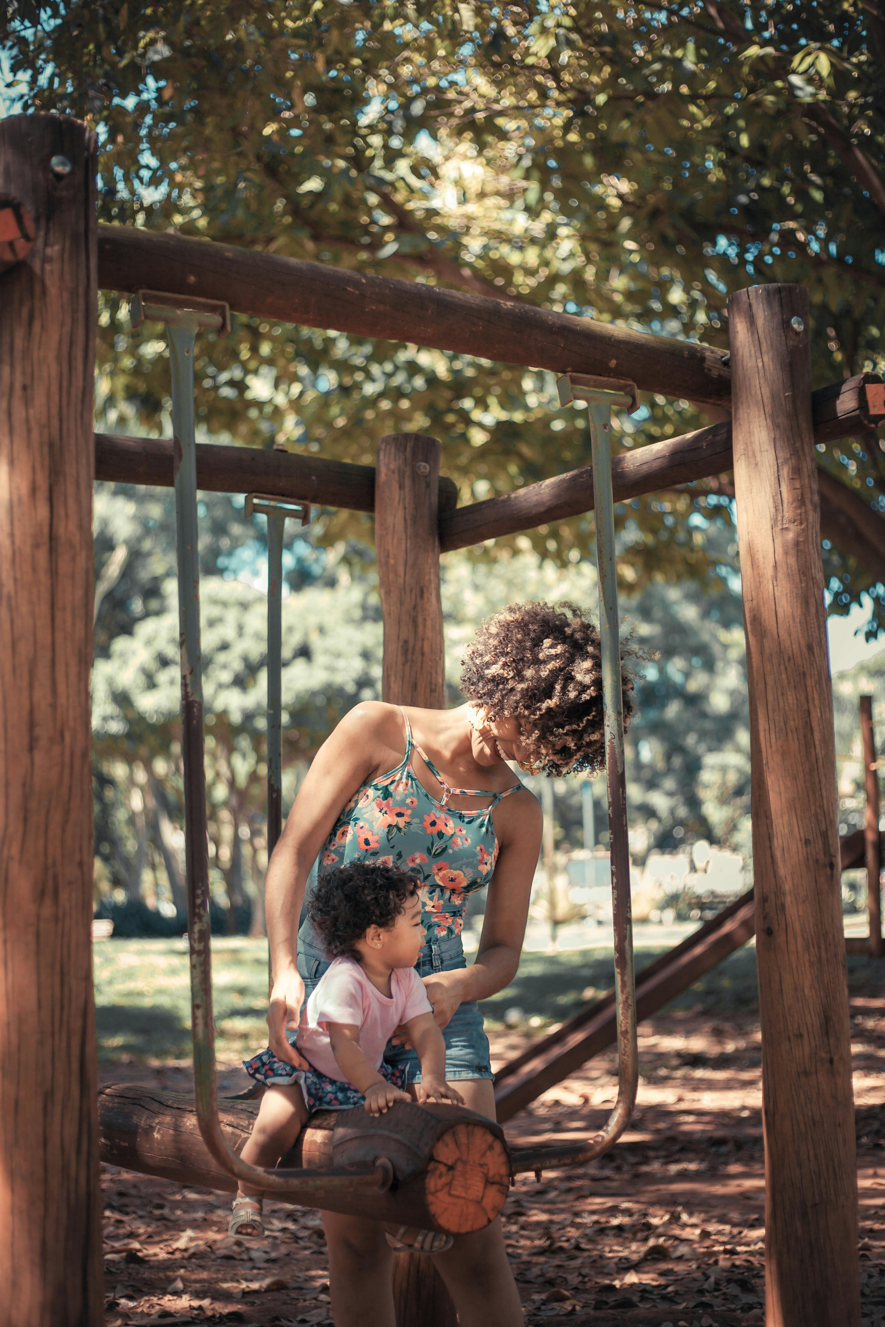 mother helping her baby girl sit on seesaw