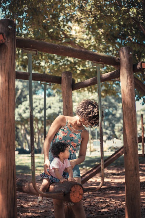 Free Mother Helping Her Baby Girl Sit on Seesaw Stock Photo