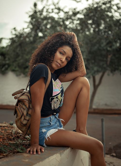 Free Urban fashion photoshoot of a stylish woman with curly hair posing outdoors on a stone railing. Stock Photo