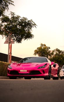 A vibrant pink Ferrari F8 captured in the streets of Dubai at dusk, showcasing luxury and urban life.