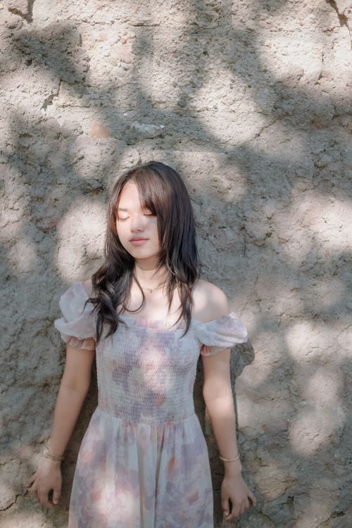 Free A woman stands against a stone wall, embraced by sunlight and shadow. Stock Photo