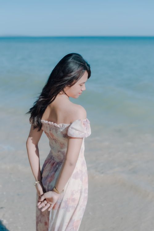 Free Elegant woman in floral dress enjoying a sunny day at the beach, relaxing by the water. Stock Photo