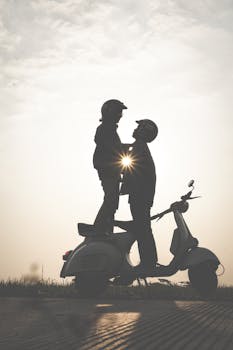 一对情侣站在摩托车旁，在夕阳下相拥成剪影