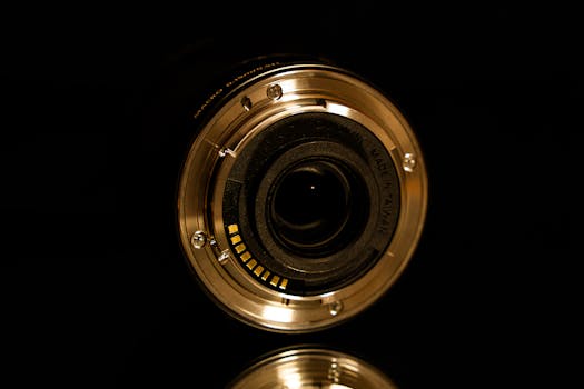Detailed close-up of a digital camera lens, showcasing its mechanical elements, on a reflective black surface.