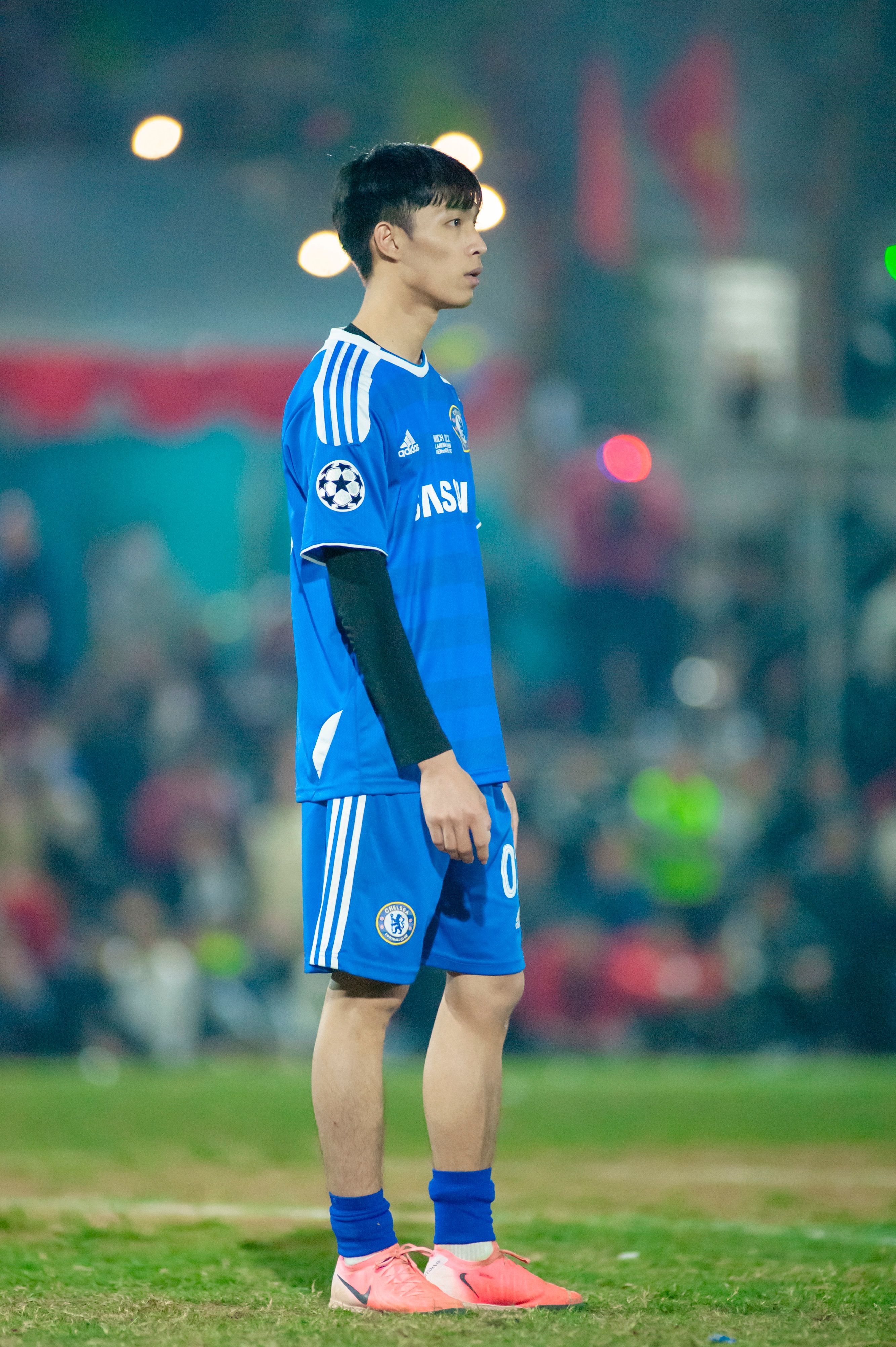 A focused young male soccer player in blue uniform on a grass field in Hà Nội, Vietnam.