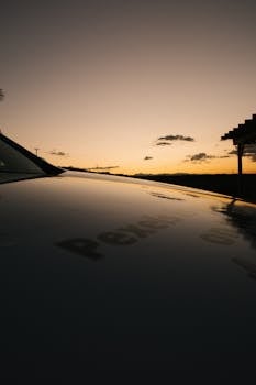 汽车引擎盖上倒映着美丽的日落天空，云彩和剪影清晰可见