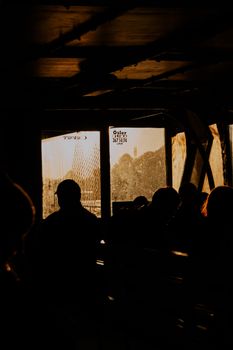Silhouettes of passengers in a dimly lit bus interior at sunset, creating a moody atmosphere.